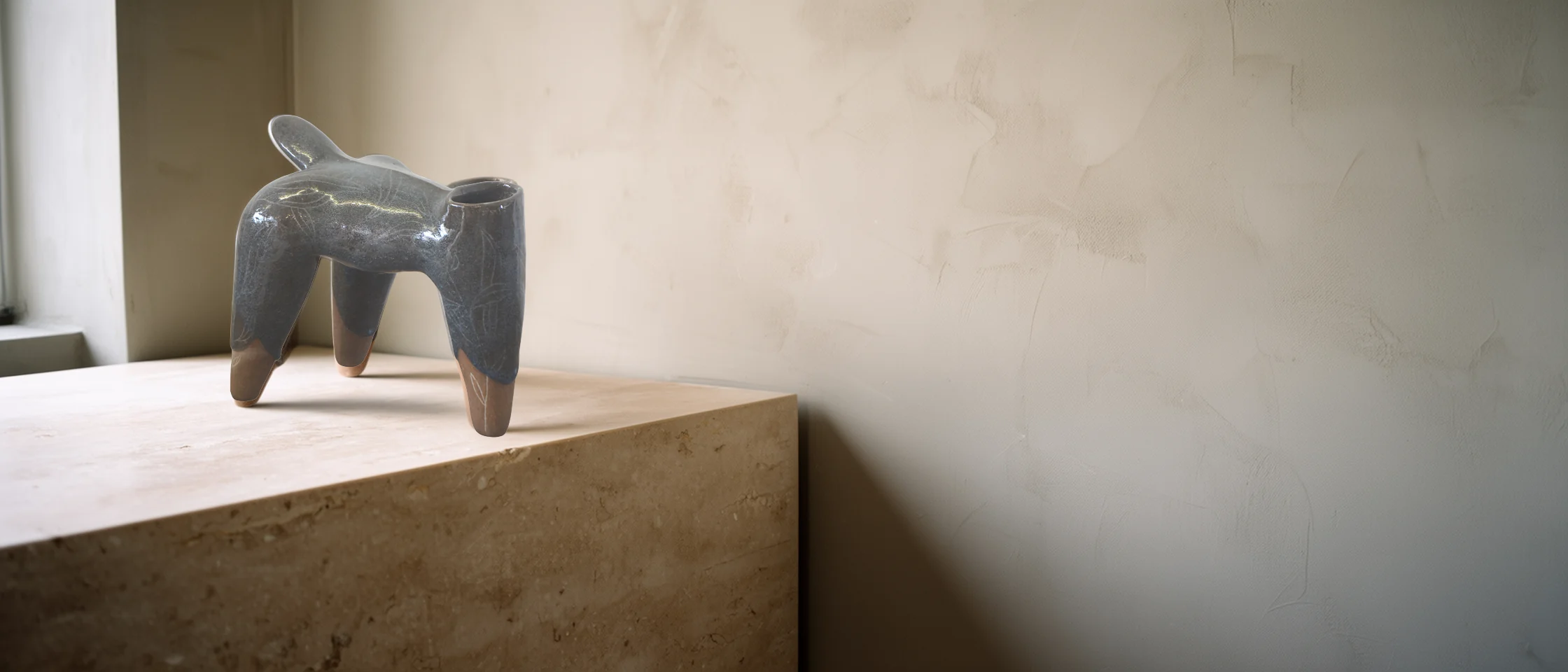 La sculpture grise brillante posée sur un socle de travertin vu de biais, près d'une fenêtre, devant un grand mur de chaux.