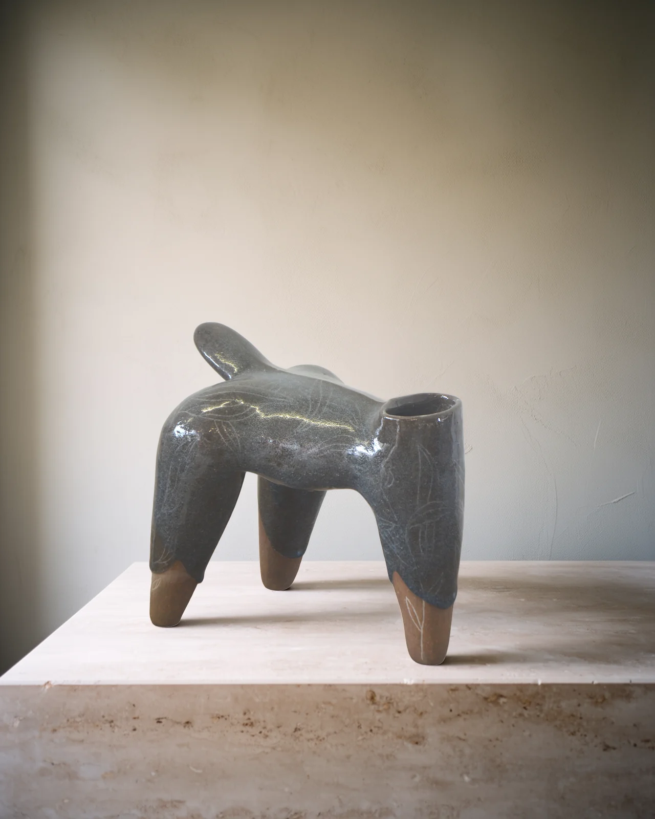 Sculpture à quatre pattes à l'émail gris brillant, pieds de terre nue, sur un socle de travertin pâle.