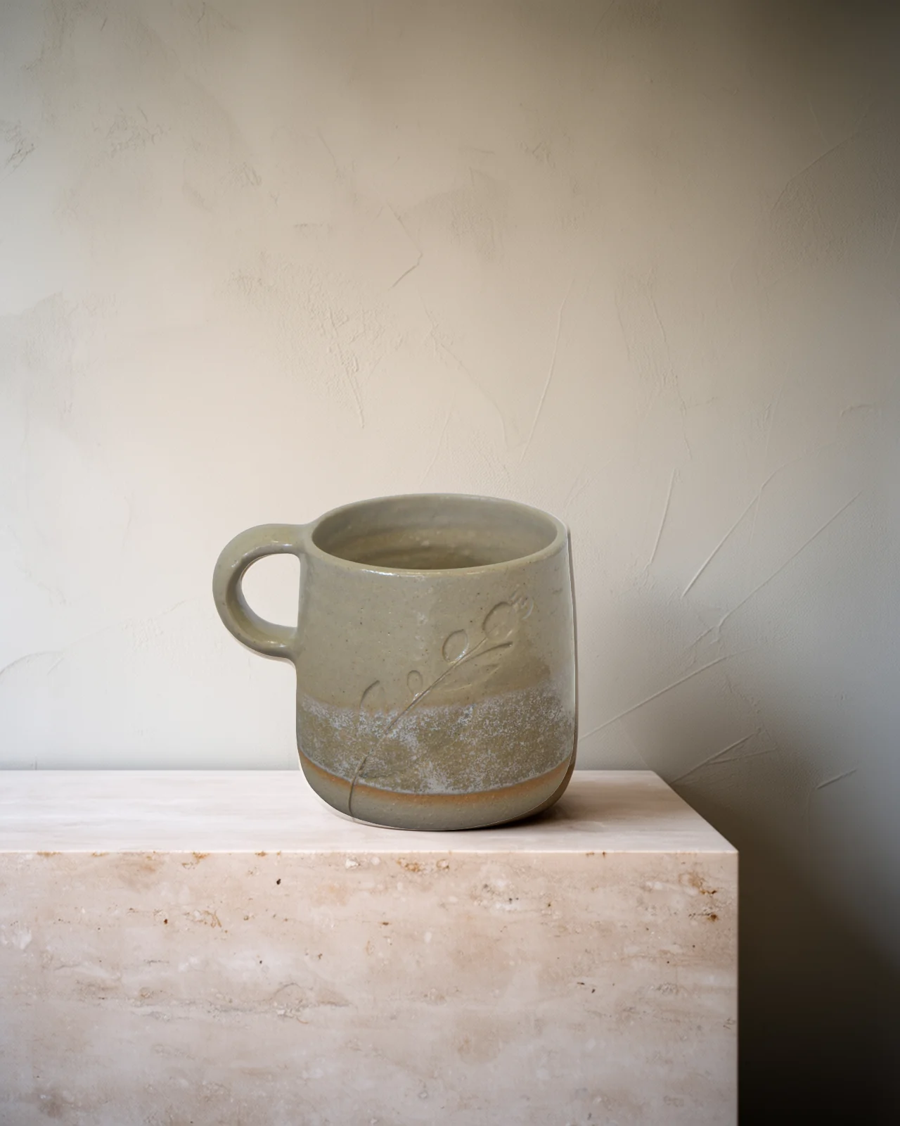 Tasse en grès gravée d'un brin, émail crème sur pied de terre nue, sur un socle de travertin pâle.