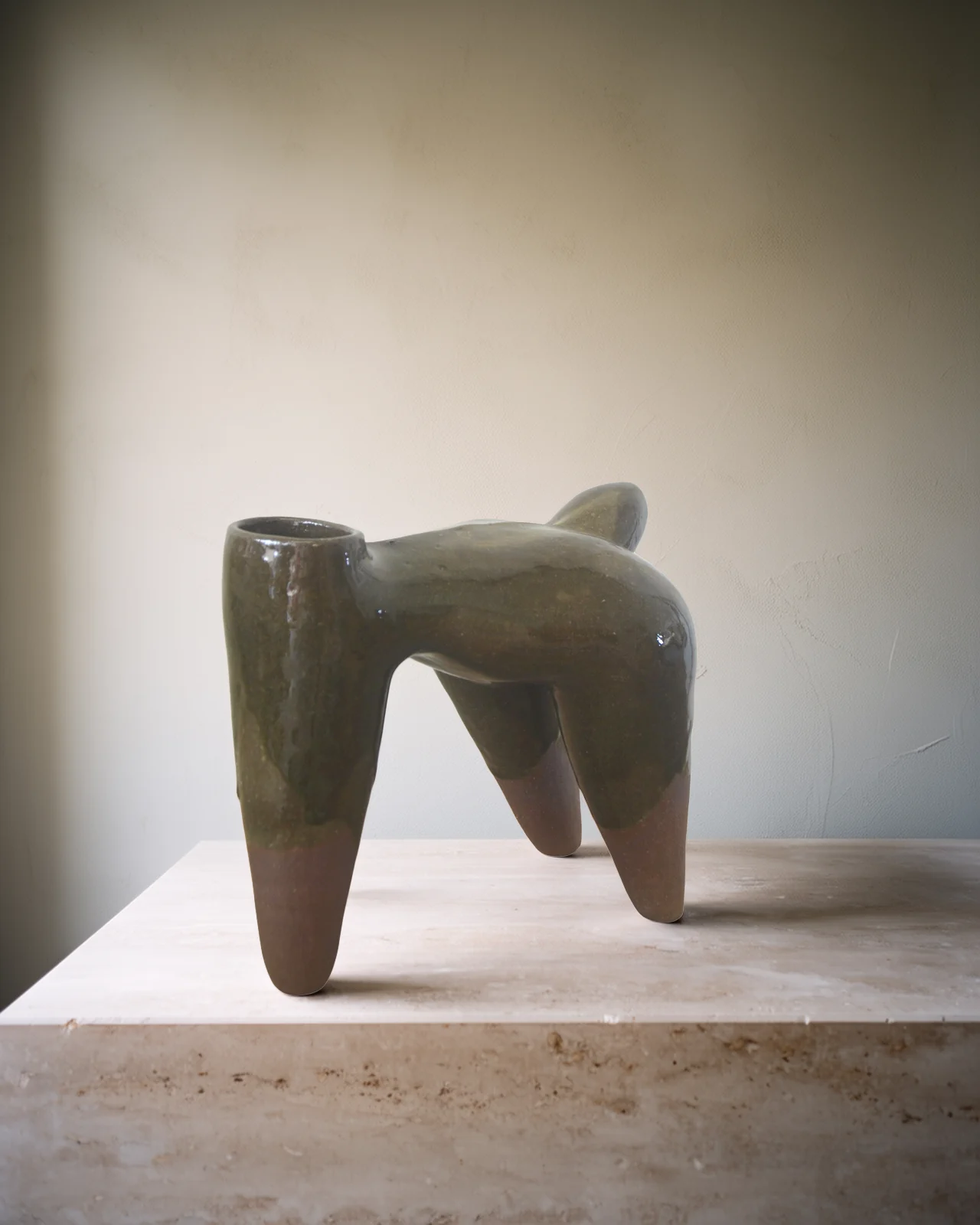 Sculpture à quatre pattes à l'émail vert-brun coulé, pieds de terre nue, sur un socle de travertin pâle.