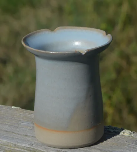 Vase en grès bleu-gris au col évasé, sur une barrière en bois.