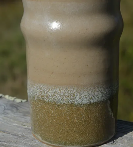Gobelet ondulé en grès, émail sable et vert, en gros plan.