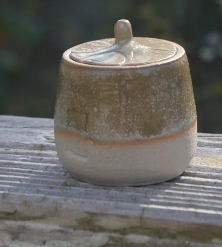Pot à couvercle en grès, émail vert olive, sur une barrière en bois.