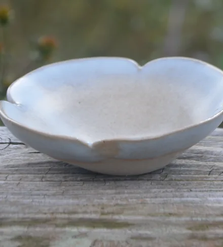 Coupelle en forme de fleur, émail blanc bleuté, sur une barrière en bois.