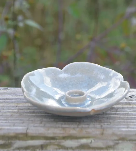 Bougeoir en forme de fleur, émail blanc bleuté, sur une barrière en bois.