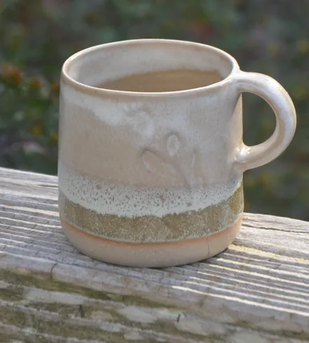 Tasse en grès, émail crème sur un pied vert, sur une barrière en bois.