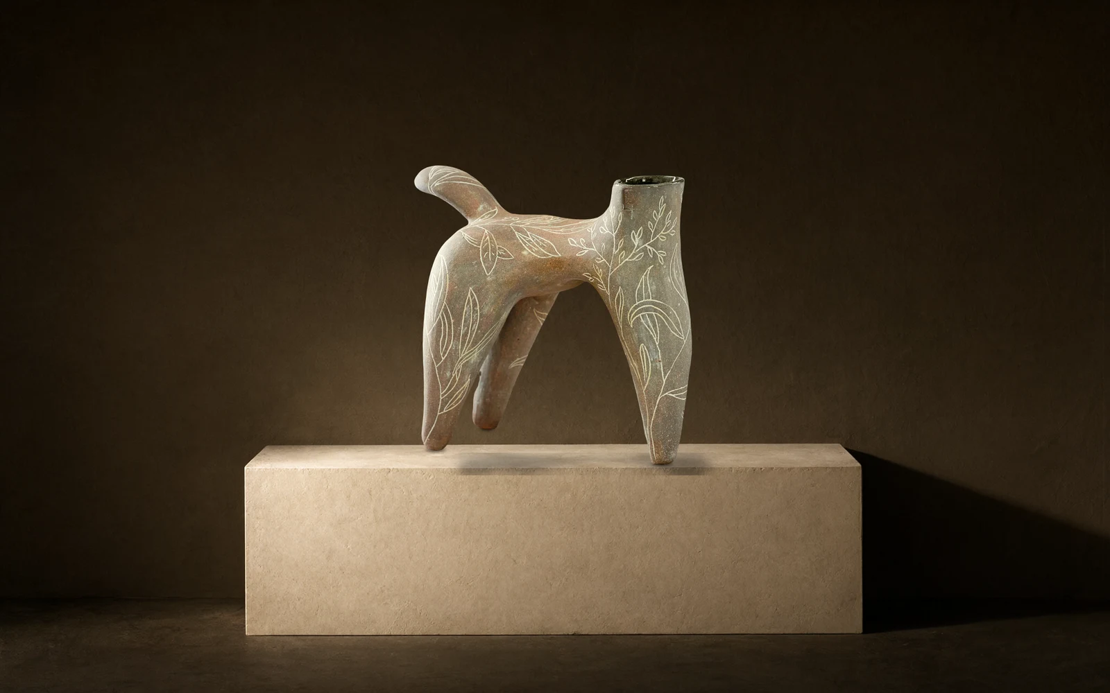 Sculpture à quatre pattes gravée de feuillages, posée sur un bloc enduit, éclairée de la gauche