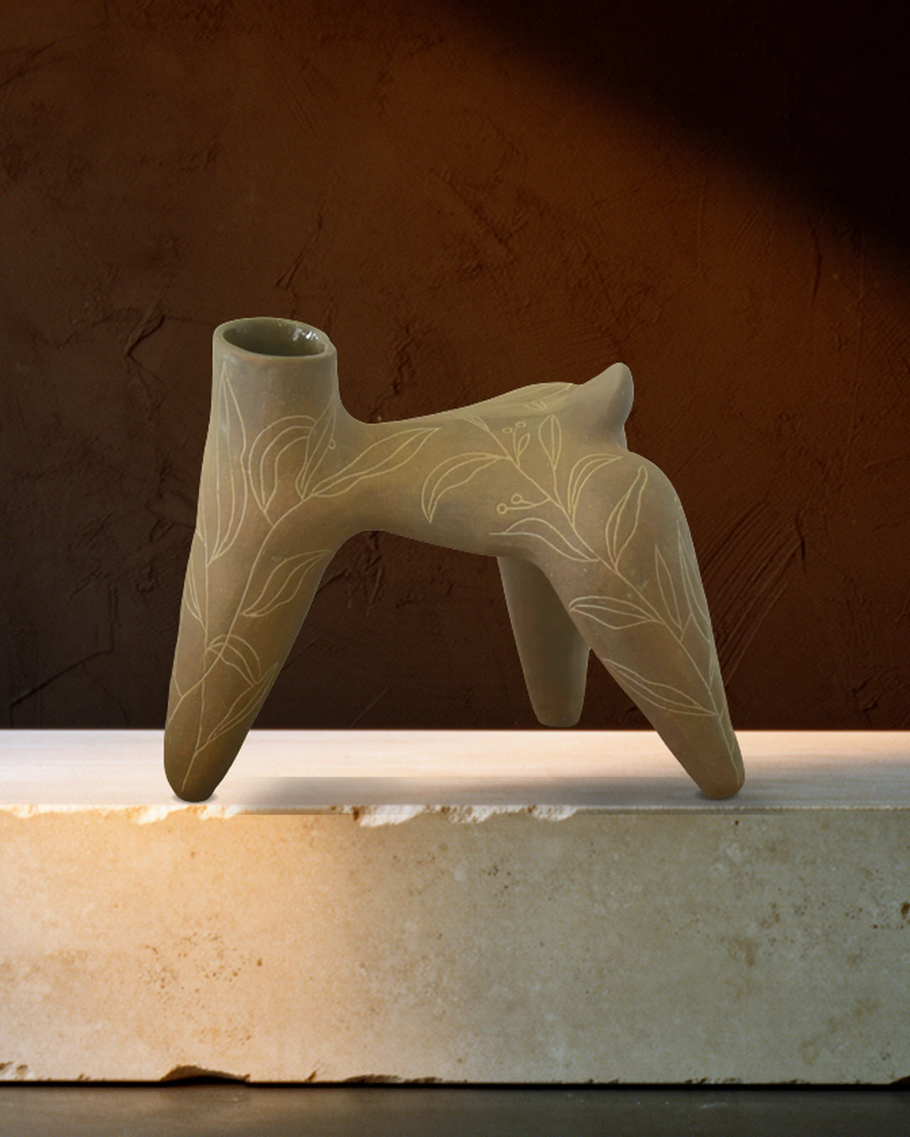Vase à quatre pattes en terre brune, gravé de feuillages, sur un socle de travertin