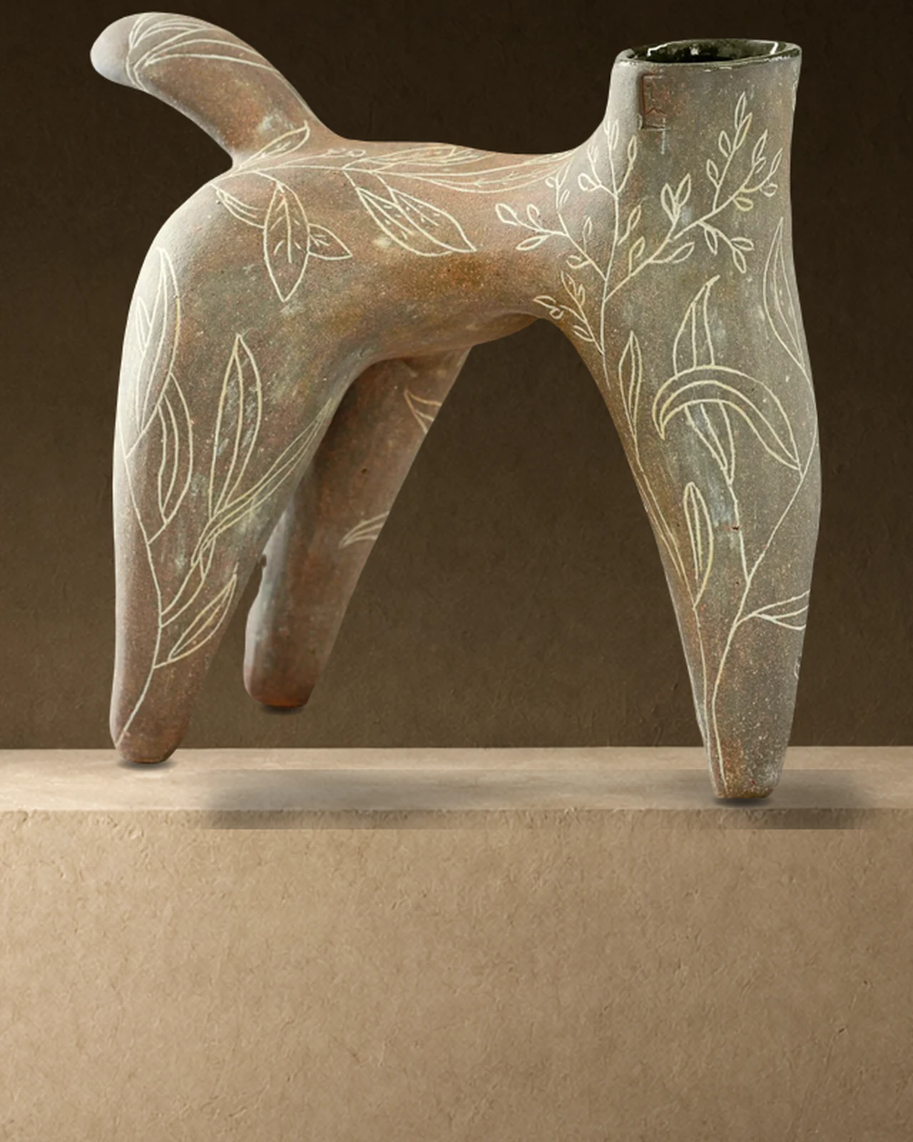 Sculpture à quatre pattes gravée de feuillages, posée sur un socle bas devant un mur sombre, éclairée de la gauche